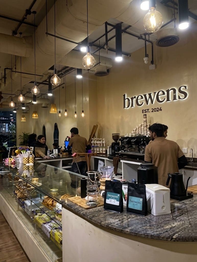 The granite coffee bar with baristas at work, pastry case and Edison bulbs overhead