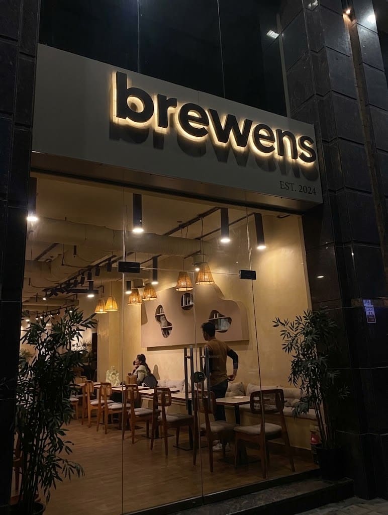 The brewens storefront at night, warm light through floor-to-ceiling glass with outdoor seating